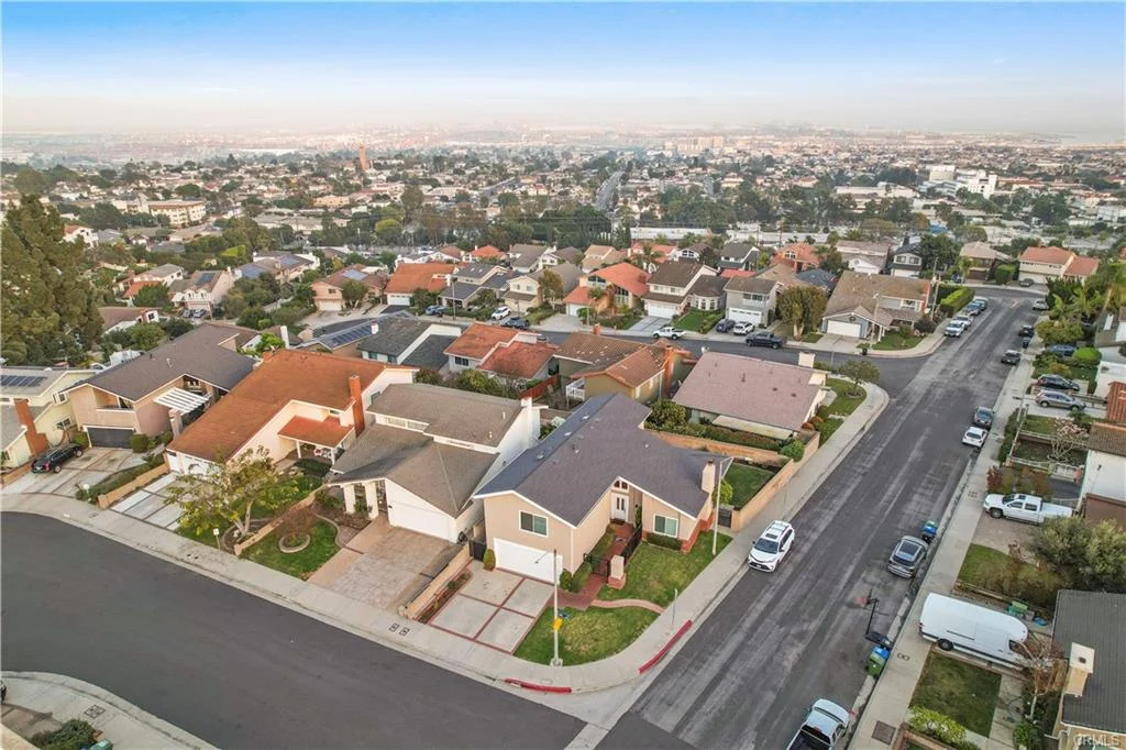 Aerial view of a suburban neighborhood featuring various houses, trees, and a street lined with parked cars.