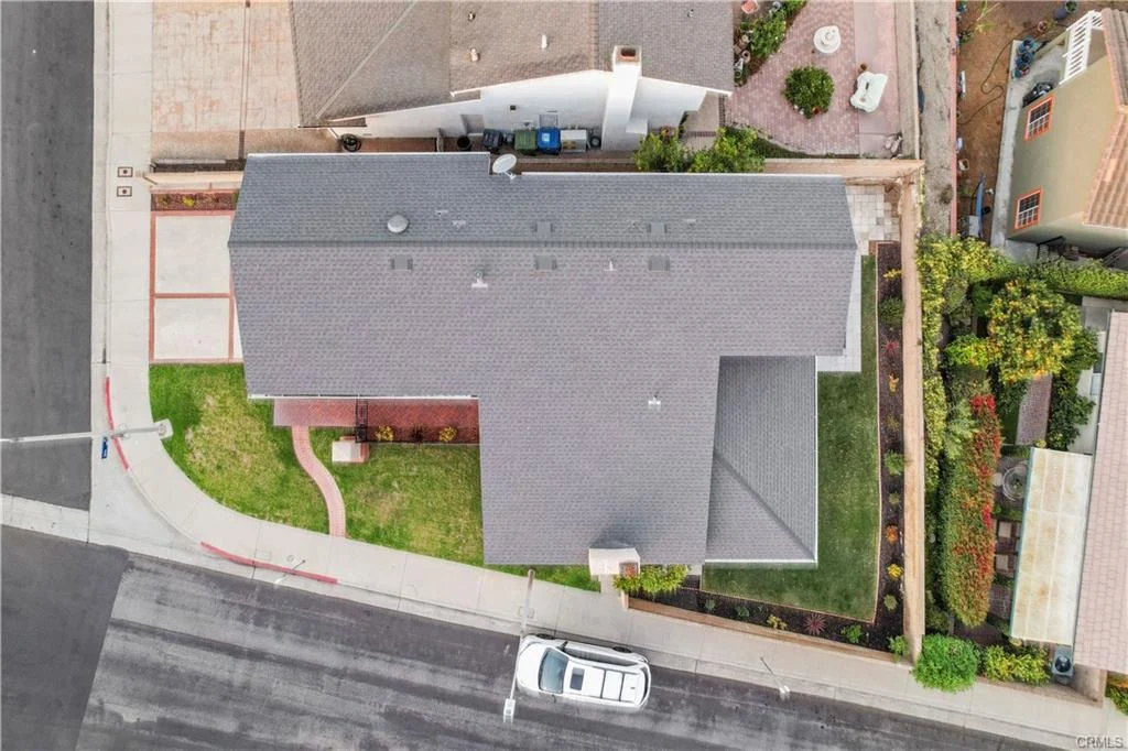 Aerial view of a suburban neighborhood featuring various houses, trees, and a street lined with parked car.