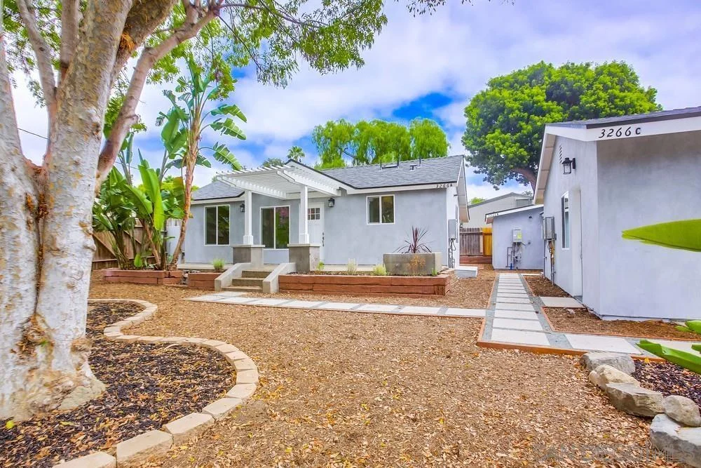 California real estate house with spacious backyard, stone path, trees, shrubs, and small patio.