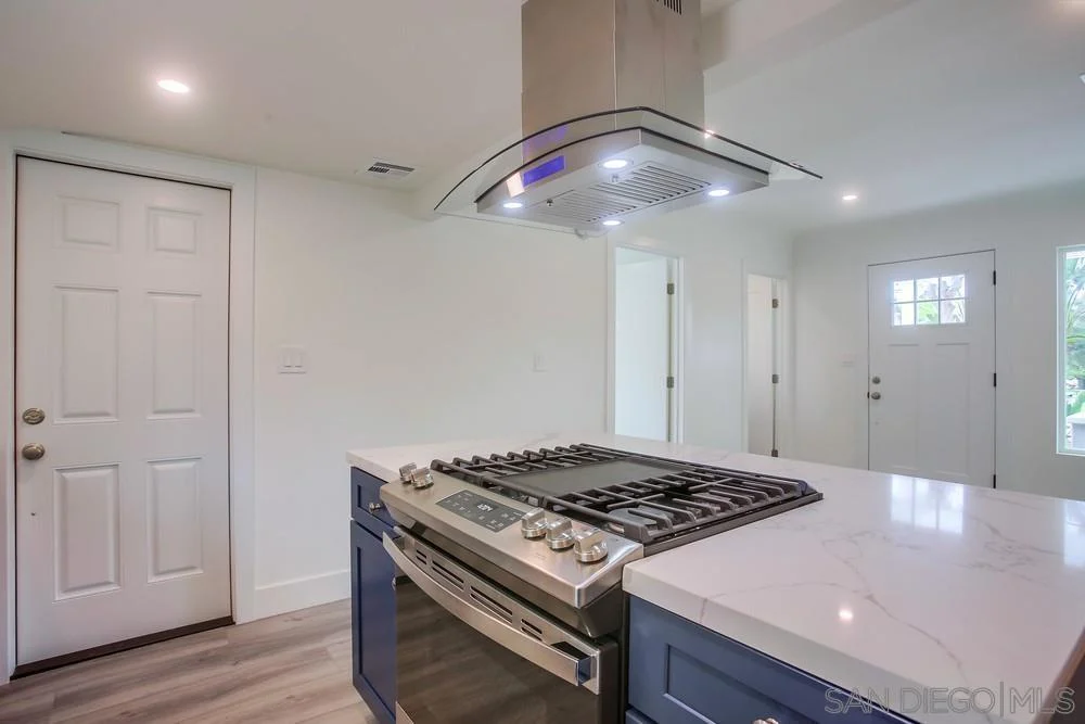 Kitchen with gas stove and hood, white walls, blue cabinets, and two doors.