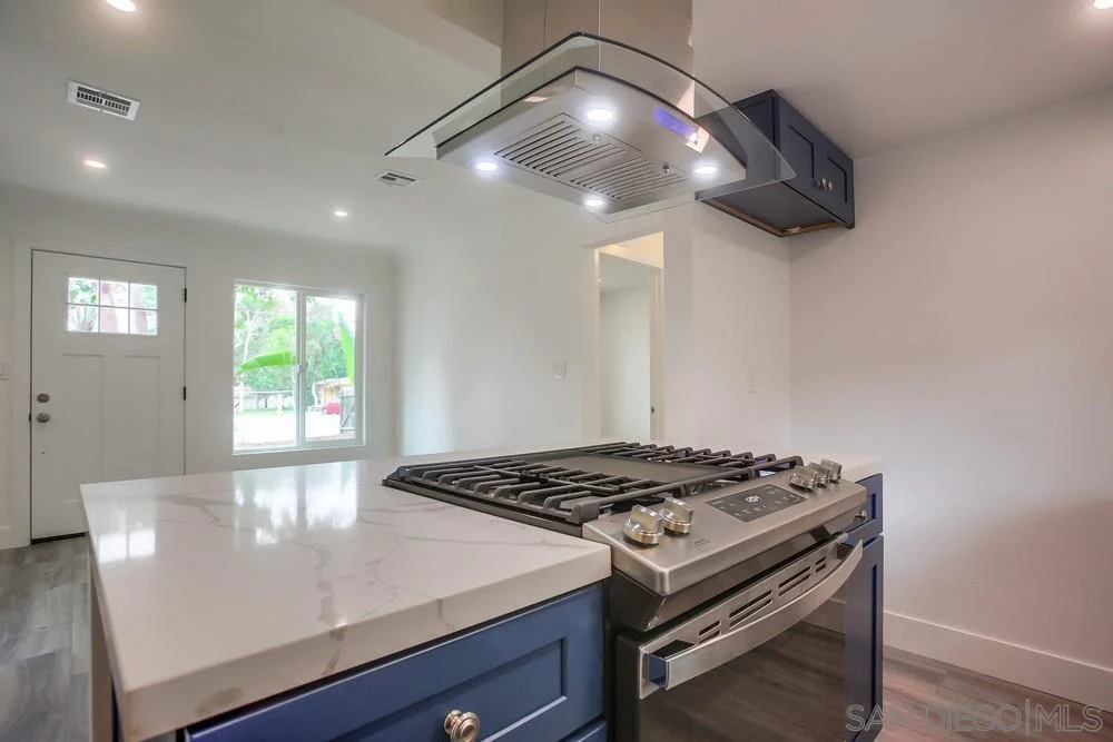 Kitchen with gas stove and hood, marble countertop, blue cabinets, door, and windows.