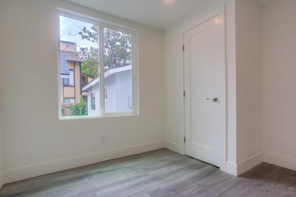 Room with light walls, large window, gray laminate floor, and door.