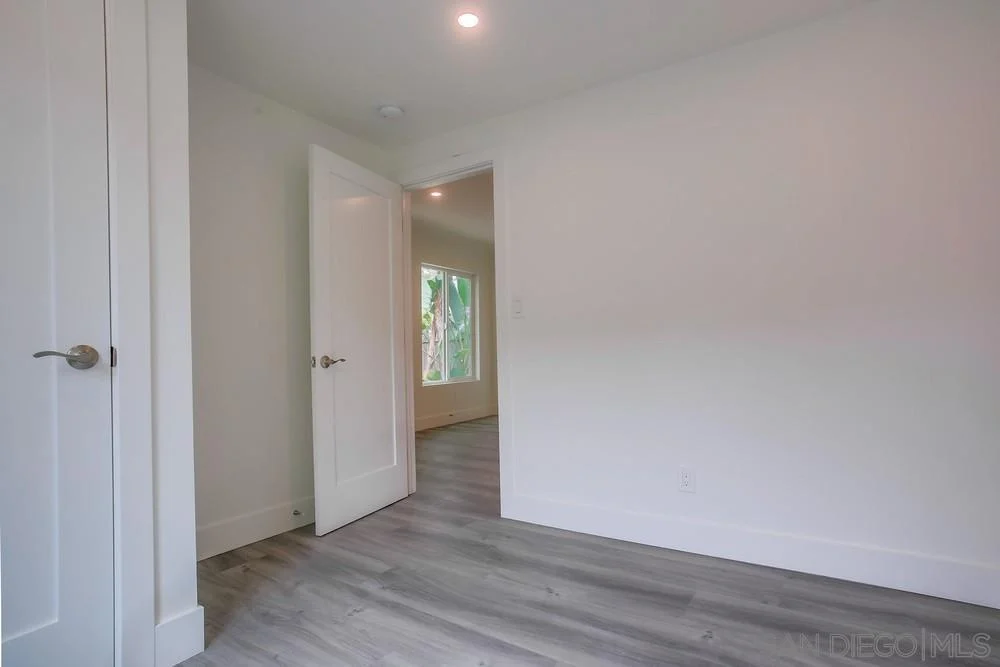 Room with light walls, wooden floor, windows, and partially open door.