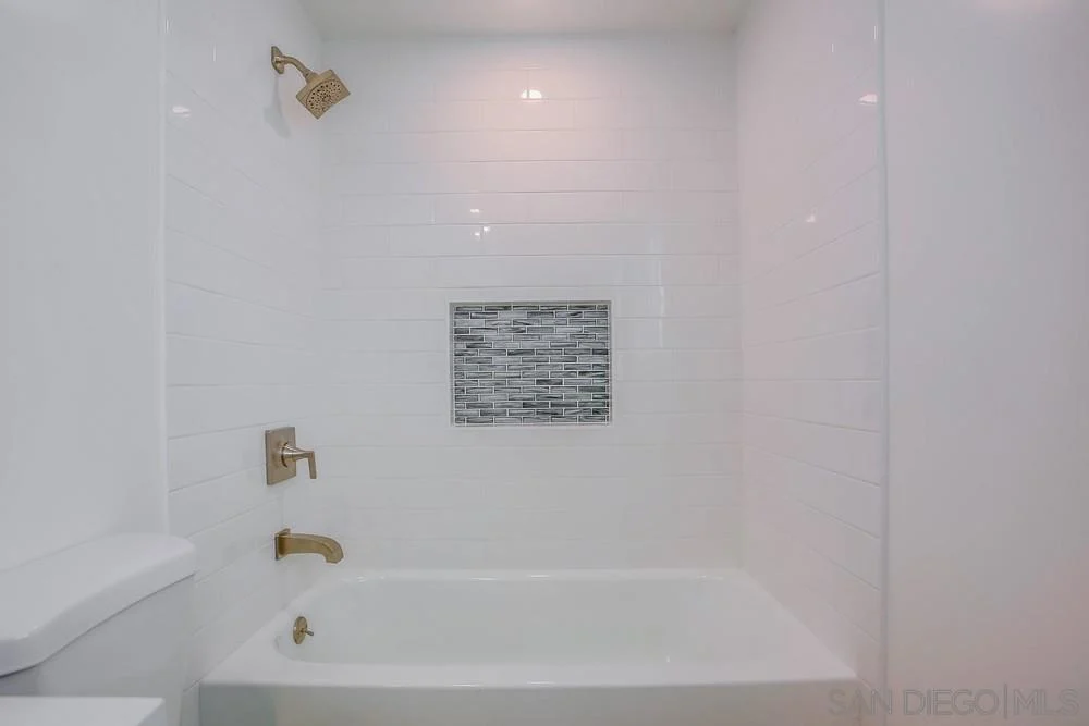 Bathroom with white tiled shower, bathtub, gold fixtures, and decorative tile inset.