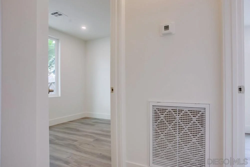 Hallway with vent, doorway, light walls, and light floor.