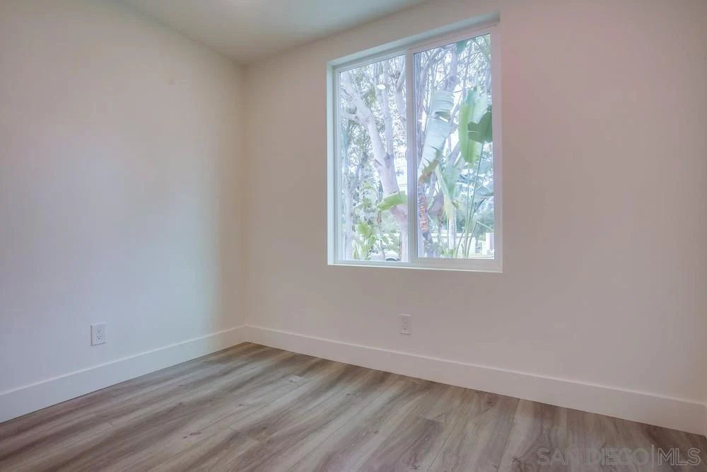Room with light walls, wooden floor, and window overlooking garden with trees.