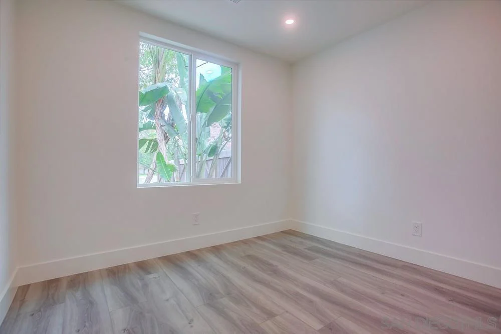 Room with light walls, window with greenery, and wooden floor.