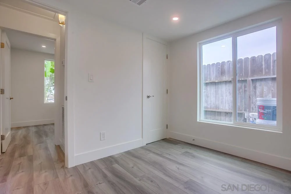 Room with white walls, large window, wooden floor, and door to another room.