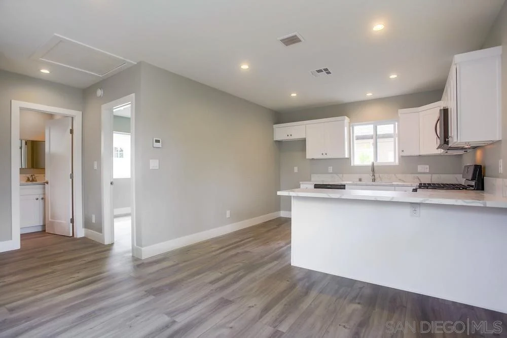 Kitchen with white cabinets, countertop, wooden floor, and doorway to another room.