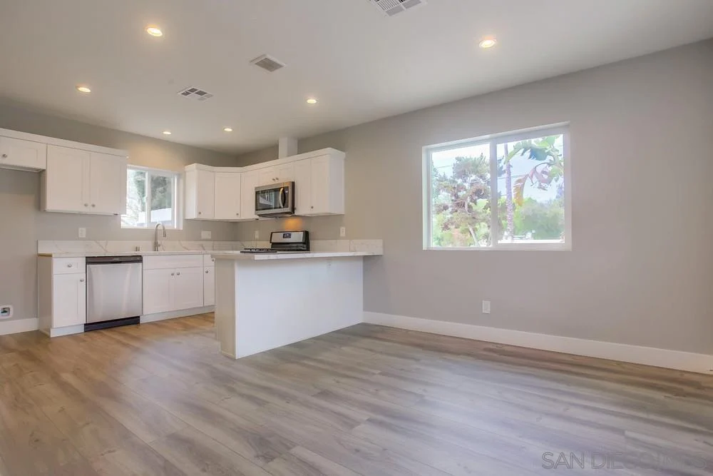 Kitchen with white cabinets, stainless steel appliances, window, and light wood floor.