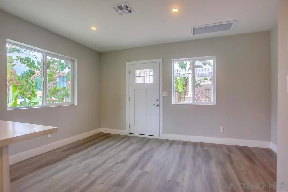Room with large windows, light walls, wooden floor, door, and small entryway.