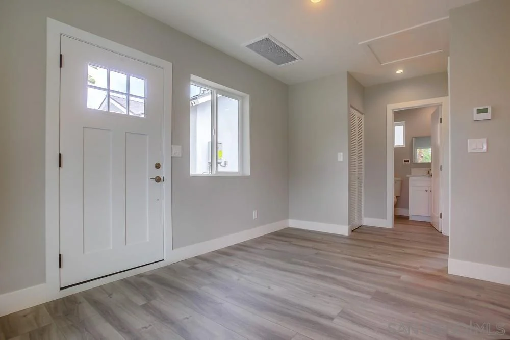 Room with light gray walls, front door, window, and wood-like floor.