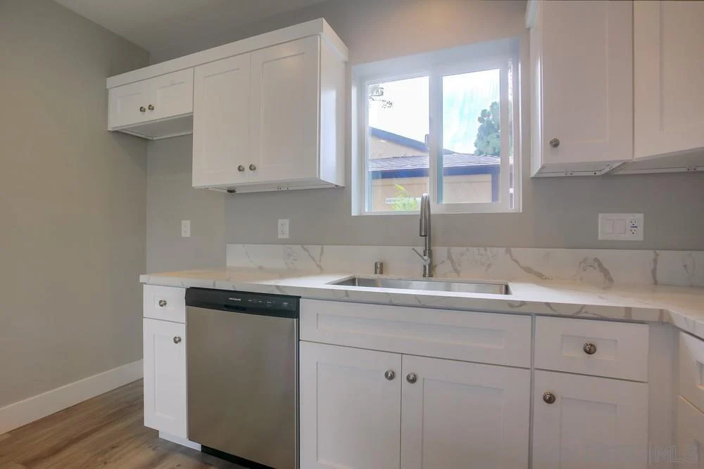 Kitchen with white cabinets, stainless steel dishwasher, and window.