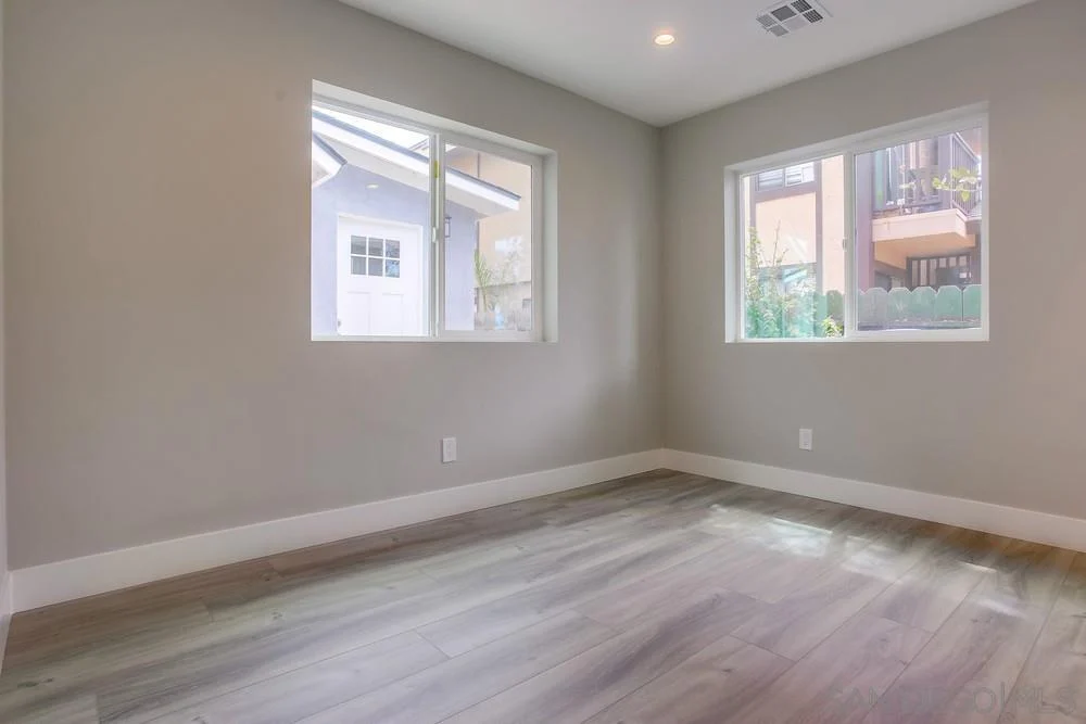 Room with light gray walls, two windows, and wooden floor.