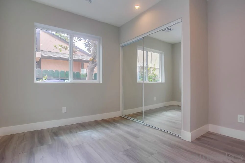 Room with light walls, large windows, mirrored closet door, and laminate floor.