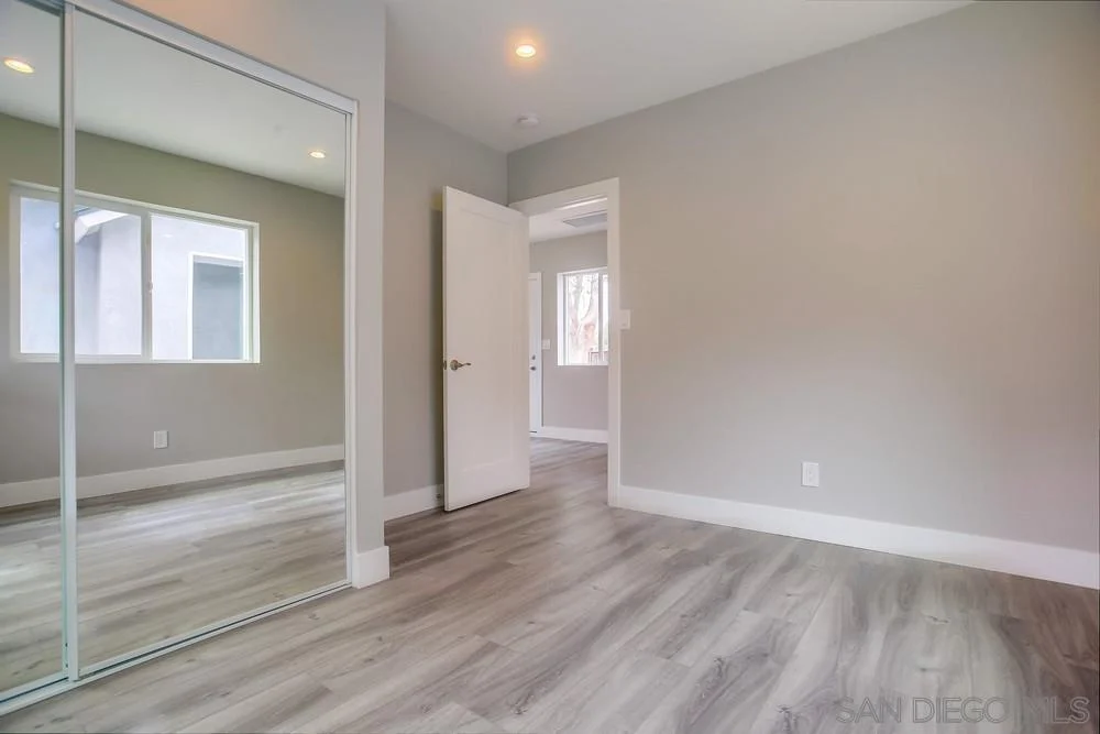 Room with gray walls, mirrored closet, large windows, light wood floor, and open door.