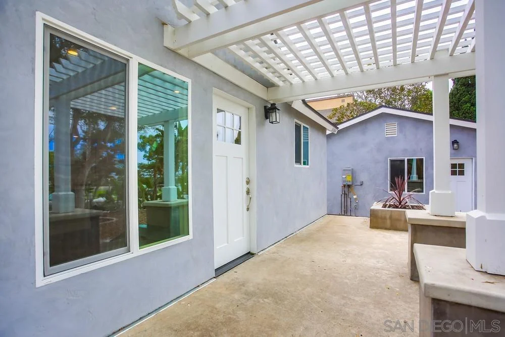 Patio with concrete floor, large windows, and overhead structure.