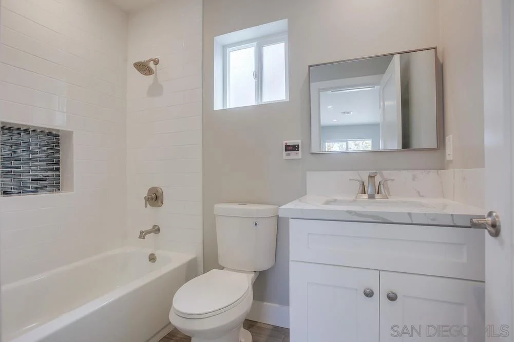 Bathroom with bathtub and shower, toilet, double sink vanity with mirror, and light gray walls.
