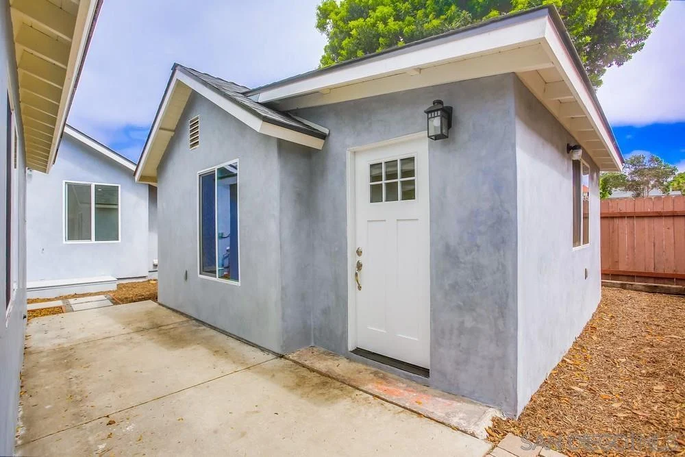 California real estate house with gray exterior, white front door and windows, concrete path, and gravel landscaping.