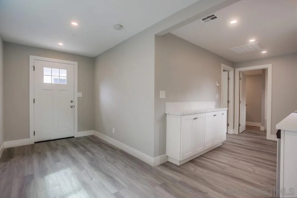 Hallway with front door, gray walls, wooden floor, white cabinet, and open doorway.