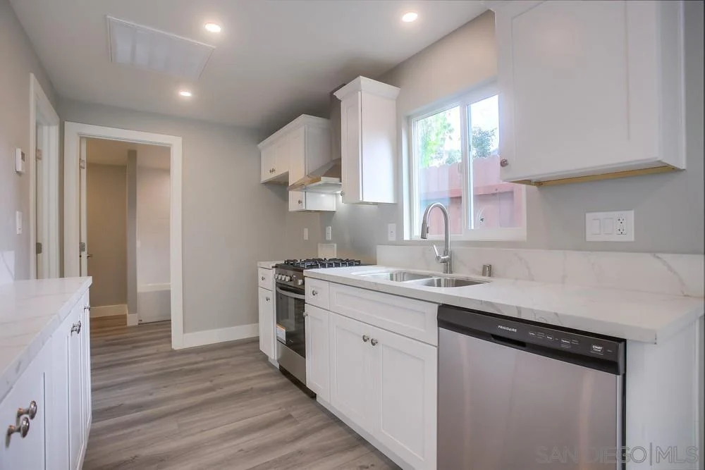 Kitchen with white cabinets, stainless steel sink, gas stove, dishwasher, light countertops, and gray walls.