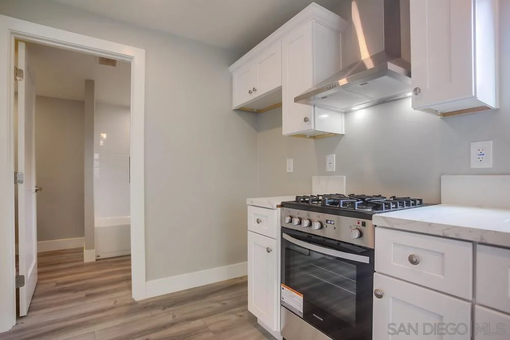 Kitchen with white cabinets, stainless steel stove and range hood, gray walls, and wood-look floor.
