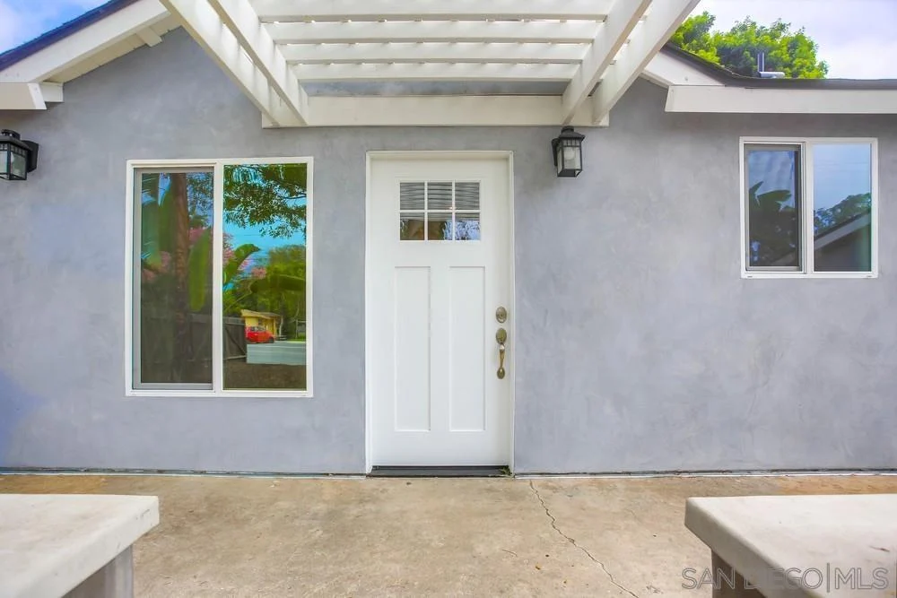 California real estate house with gray exterior, white door, large windows, and pergola above entrance.