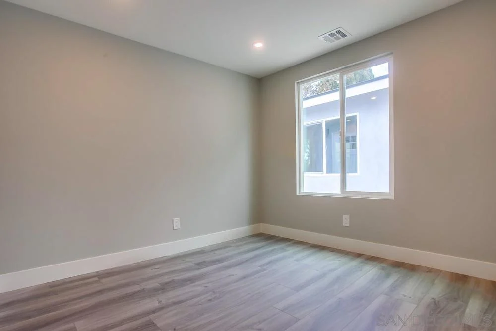 Room with light walls, window, and gray wood-like floor.