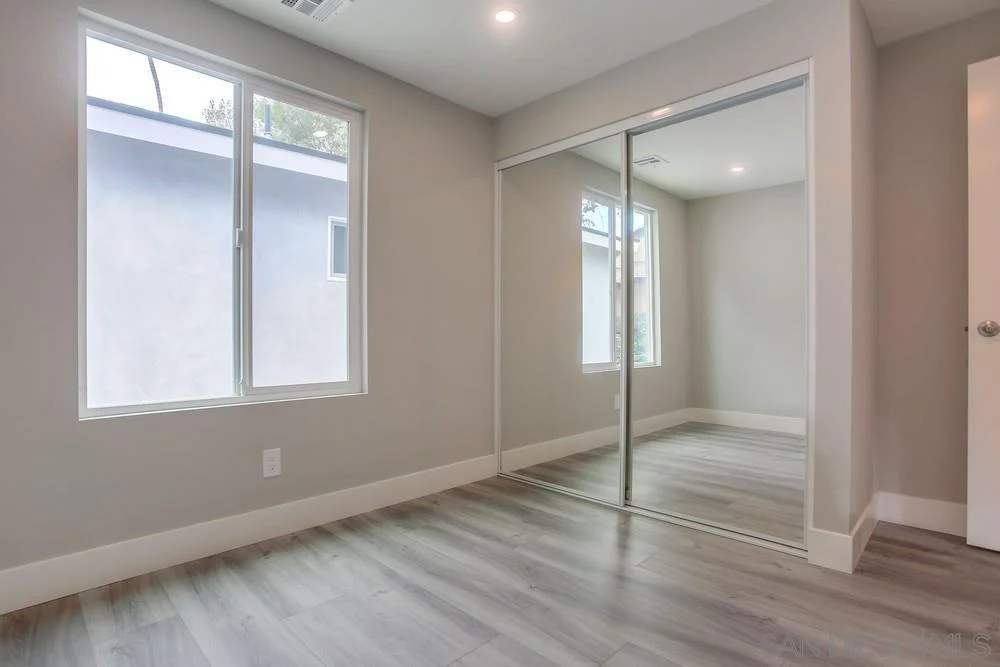 Room with gray walls, large windows, mirrored closet, and light wood floor.