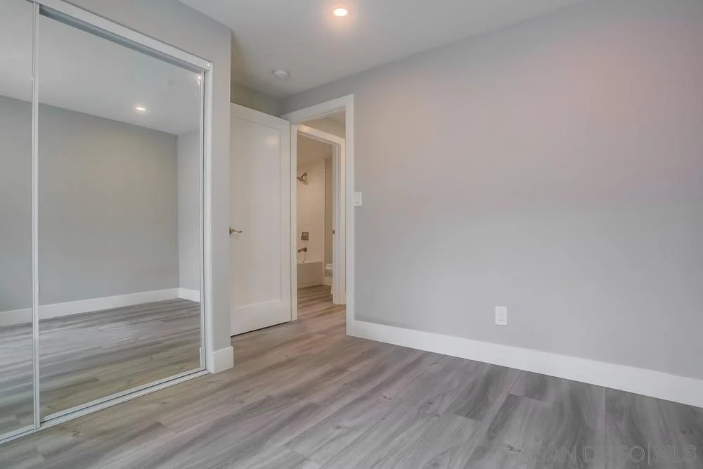 Room with gray walls, mirrored closet door, light floor, and open door to bathroom.