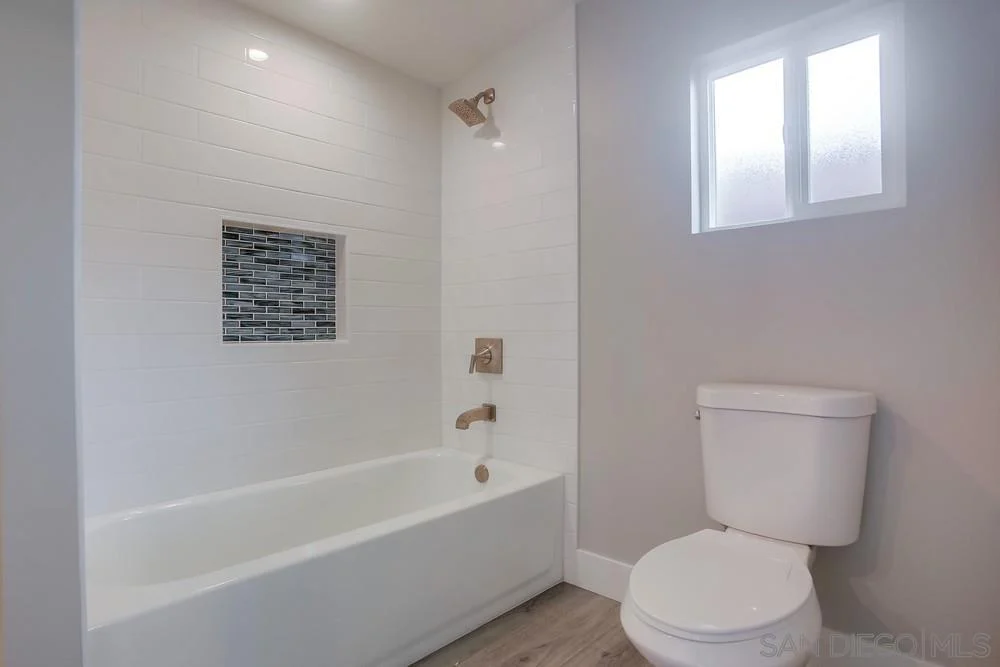 Bathroom with bathtub, tiled wall, shower, white toilet, and small window.