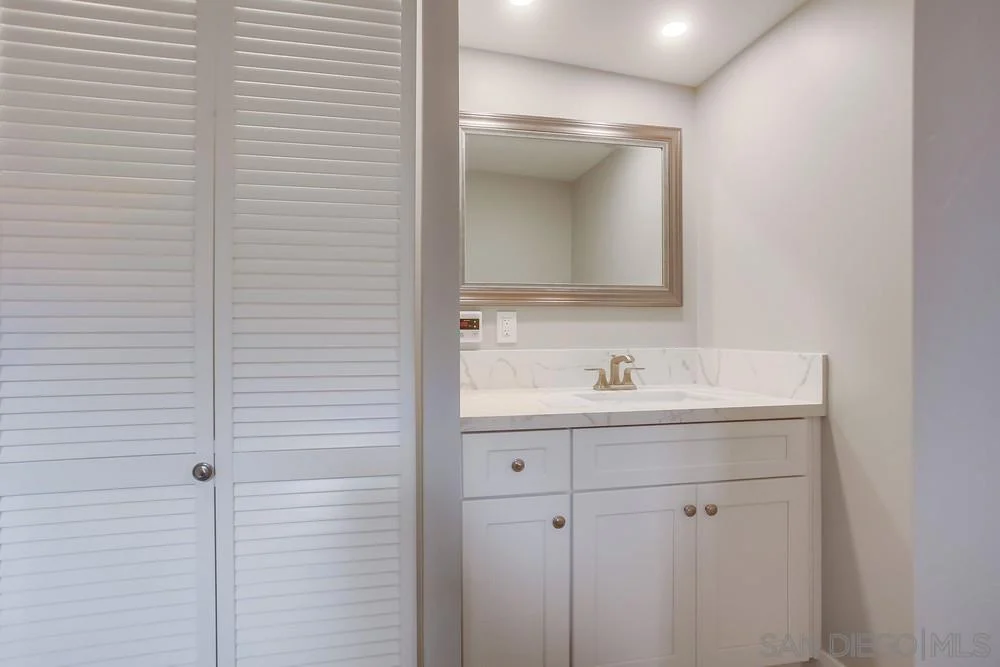 Bathroom with white cabinets, mirror, lights, and simple doors.