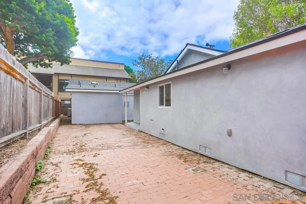 Paved area behind house with gray walls.