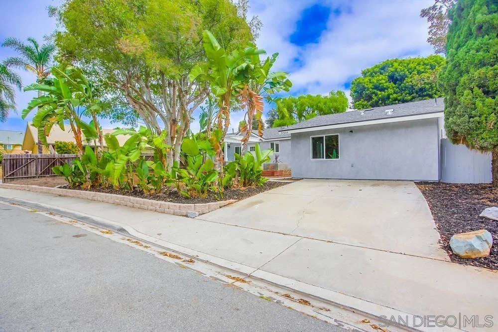 California real estate house with driveway, landscaping, trees, and plants along street.
