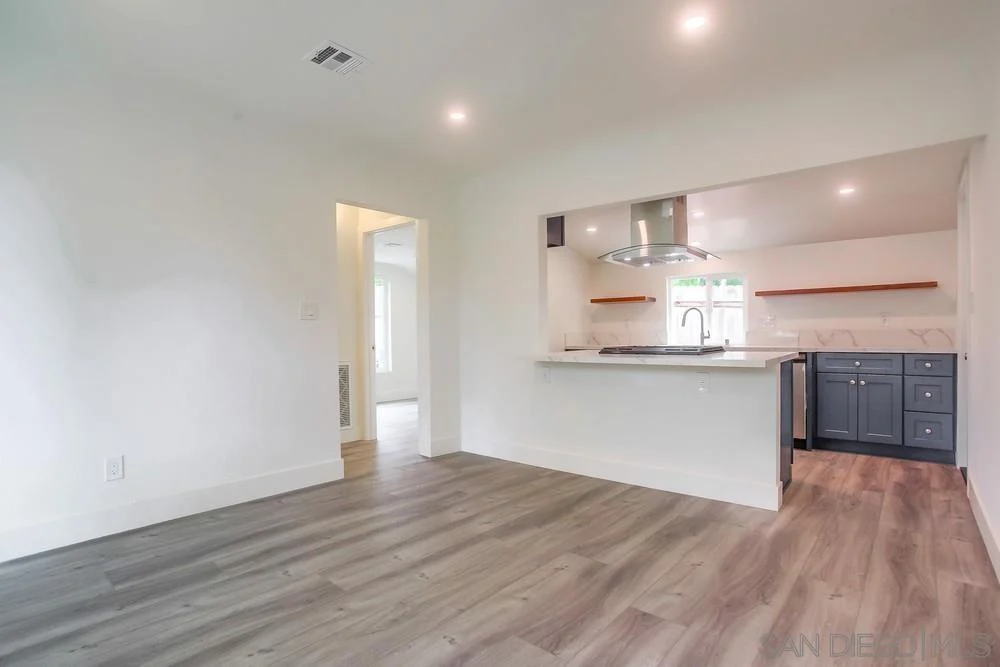 Kitchen and living area with light walls, hardwood floor, and kitchen island with stove.