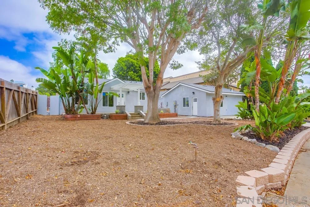 California real estate house with yard, grass, trees, and garden bed.