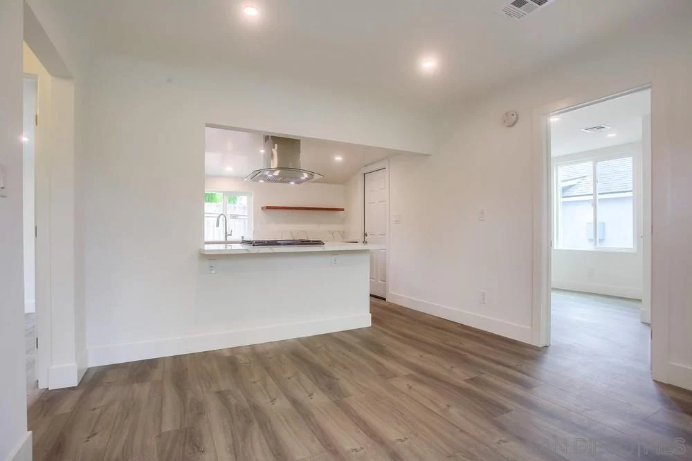 Kitchen and living area with light walls and hardwood floor.