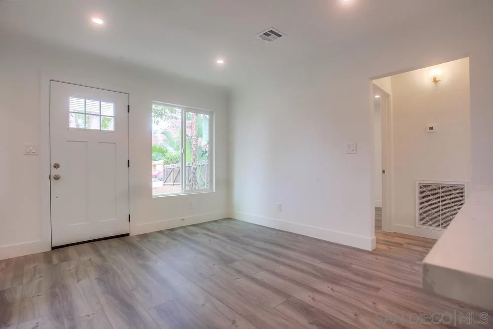Living room with white walls, light wood floor, front door with windows, and large window.