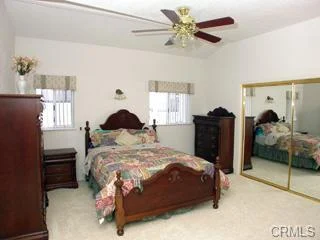 Bedroom with wooden bed, quilt, windows, ceiling fan, closet doors, dresser, and nightstand