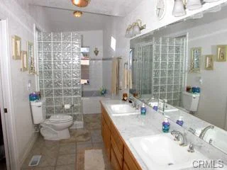 Bathroom with double sinks, cabinets, mirror, toilet, shower, and tile floor