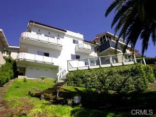 House in California real estate with balconies, windows, hillside, palm trees, and shrubs