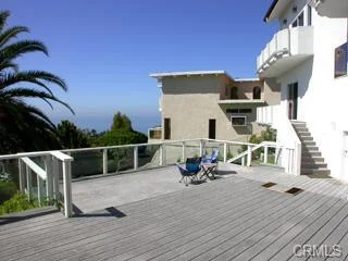 Deck with chairs, palm trees, ocean view, and exterior of house in California real estate