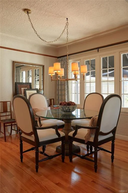 Dining room with glass table, four chairs, chandelier, and large windows.