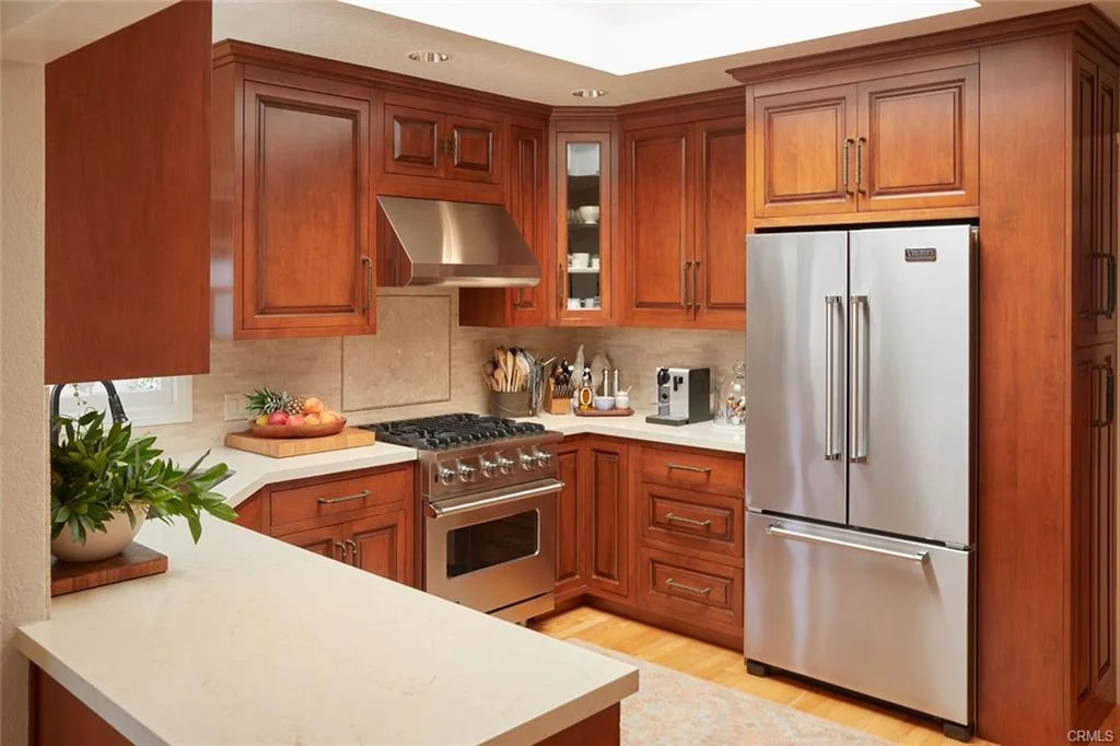 Kitchen with wooden cabinets, stainless steel fridge, gas stove with oven, and countertop.
