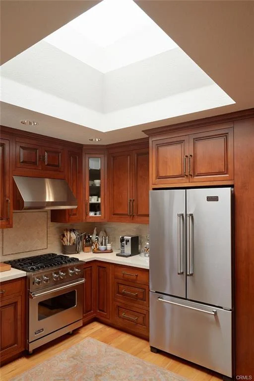 Kitchen with wooden cabinets, stainless steel fridge, and gas stove with range hood.