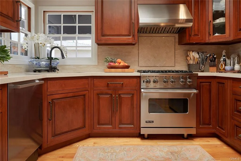 Kitchen with wooden cabinets, stainless steel stove, fruit on countertop, and window.