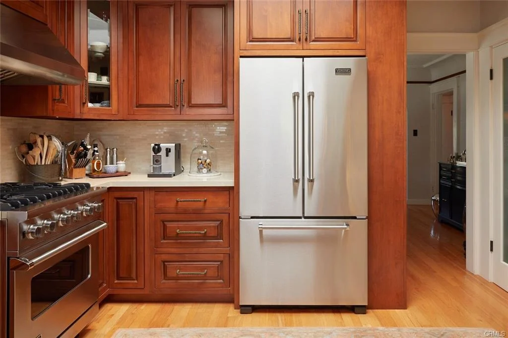 Kitchen with wooden cabinets, stainless steel fridge, gas stove, and small appliances.