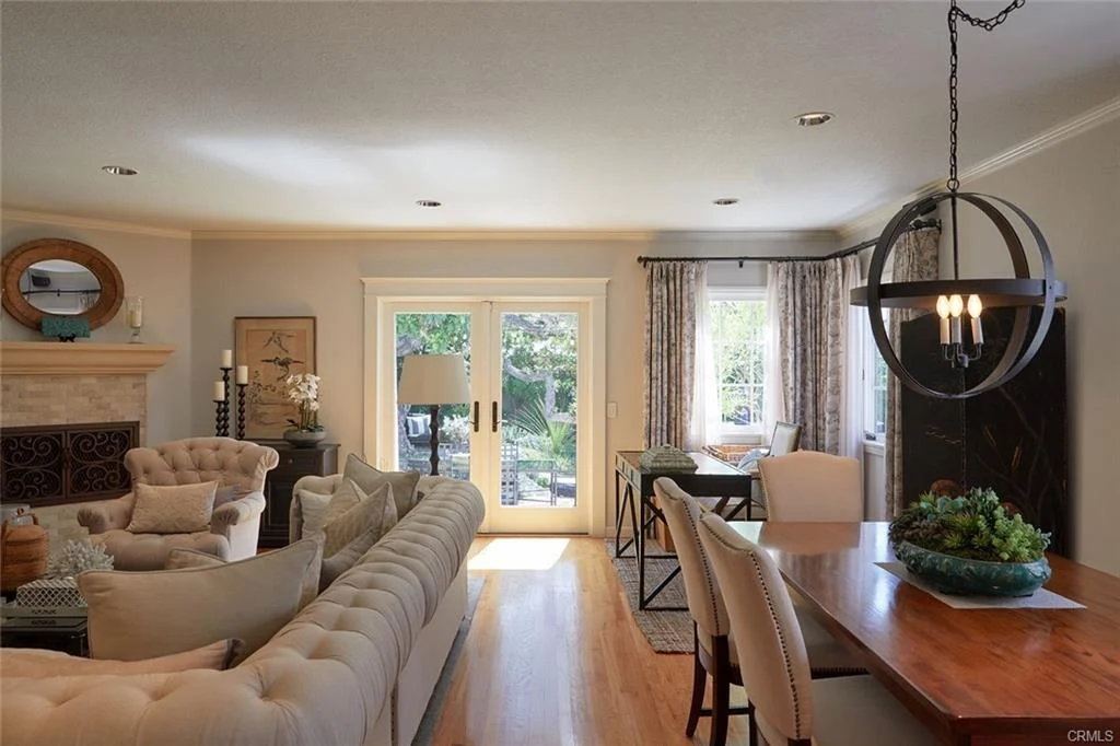 Living room with cream sofa, fireplace, large windows, and dining area with wooden table.