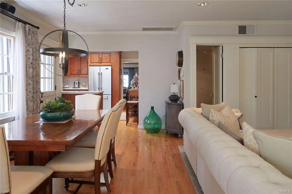 Dining area with wooden table, white chairs, green vase, and open layout to kitchen and living area.