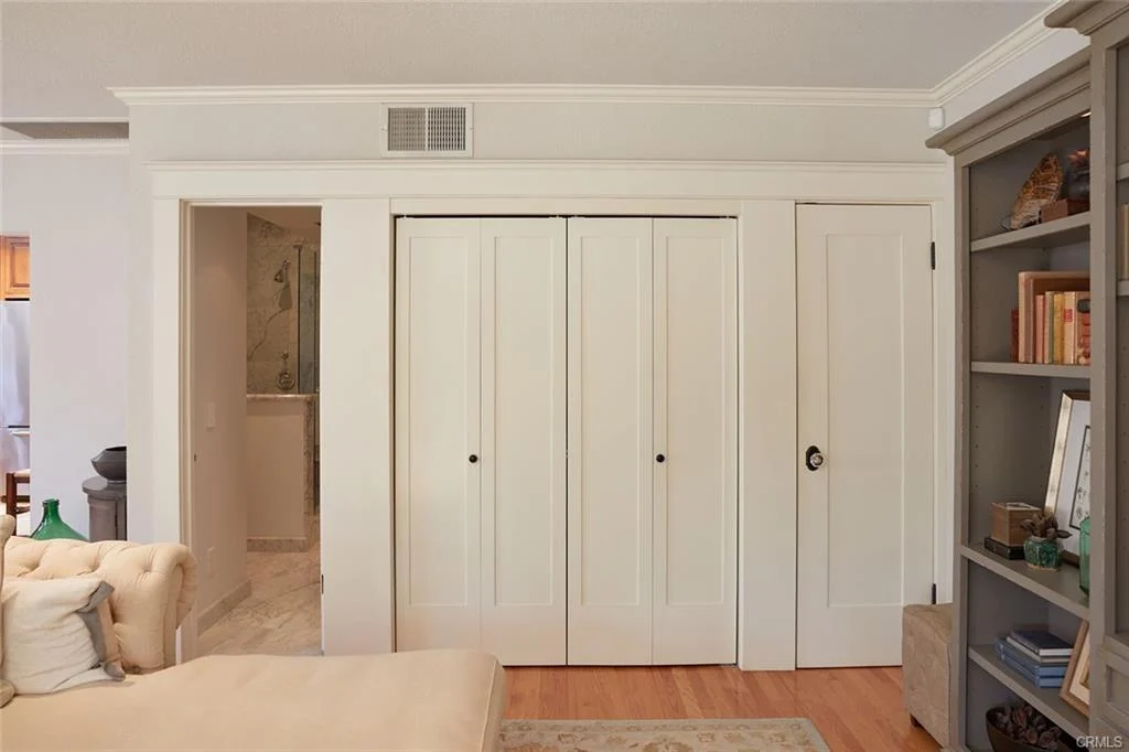 Room with beige sofa, white closet doors, and gray bookshelf with books and decor.